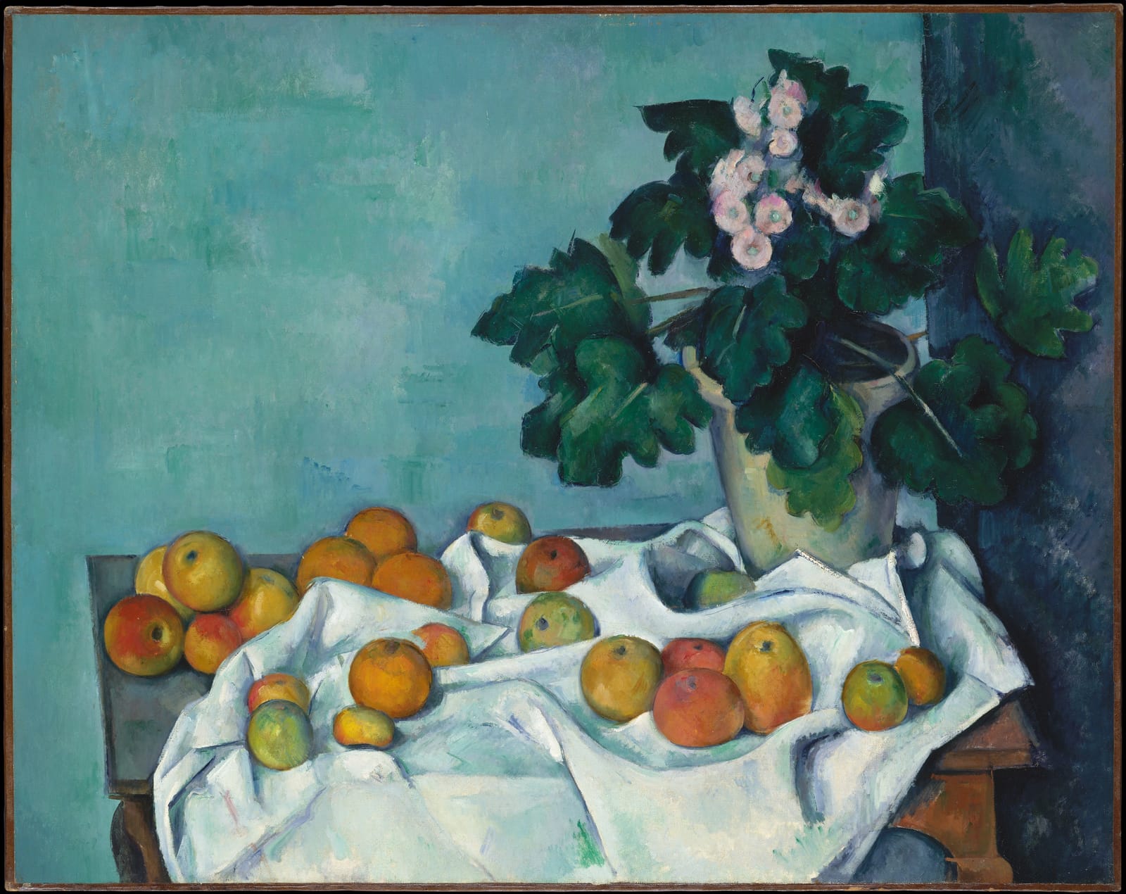 Apples on a white cloth beside a pot of primroses on a wooden table.