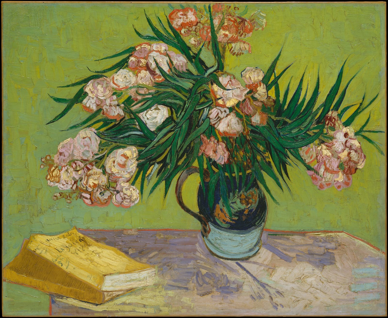 Pink oleanders in a jug beside a yellow book, on a table painted in vivid green and yellow.
